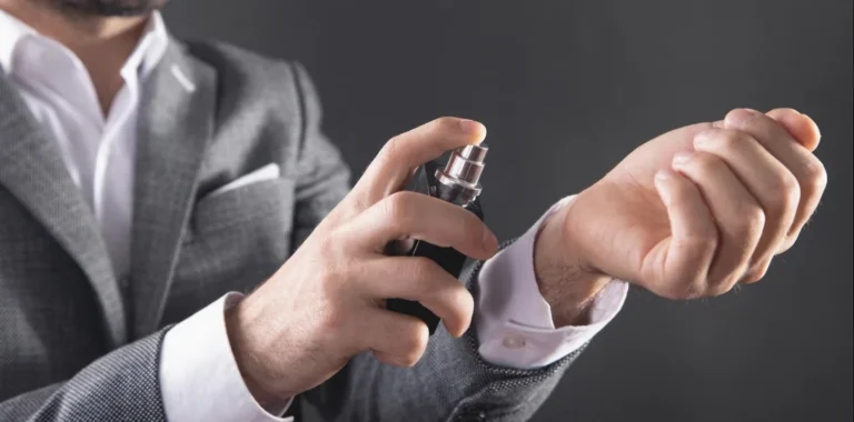 Un homme en costume gris vaporise du parfum sur l'intérieur de son poignet.