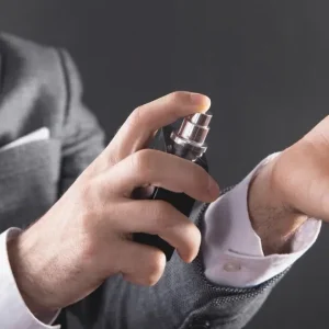 Un homme en costume gris vaporise du parfum sur l'intérieur de son poignet.